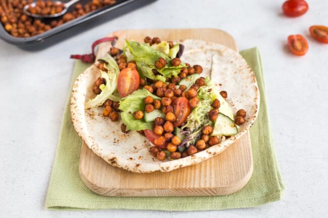 wrap op een houten snijplank, gegarneerd met salade en kruidig geroosterde kikkererwten.