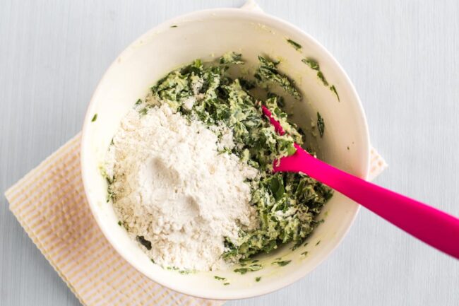 Spinach and ricotta dumpling mixture in a bowl with added flour