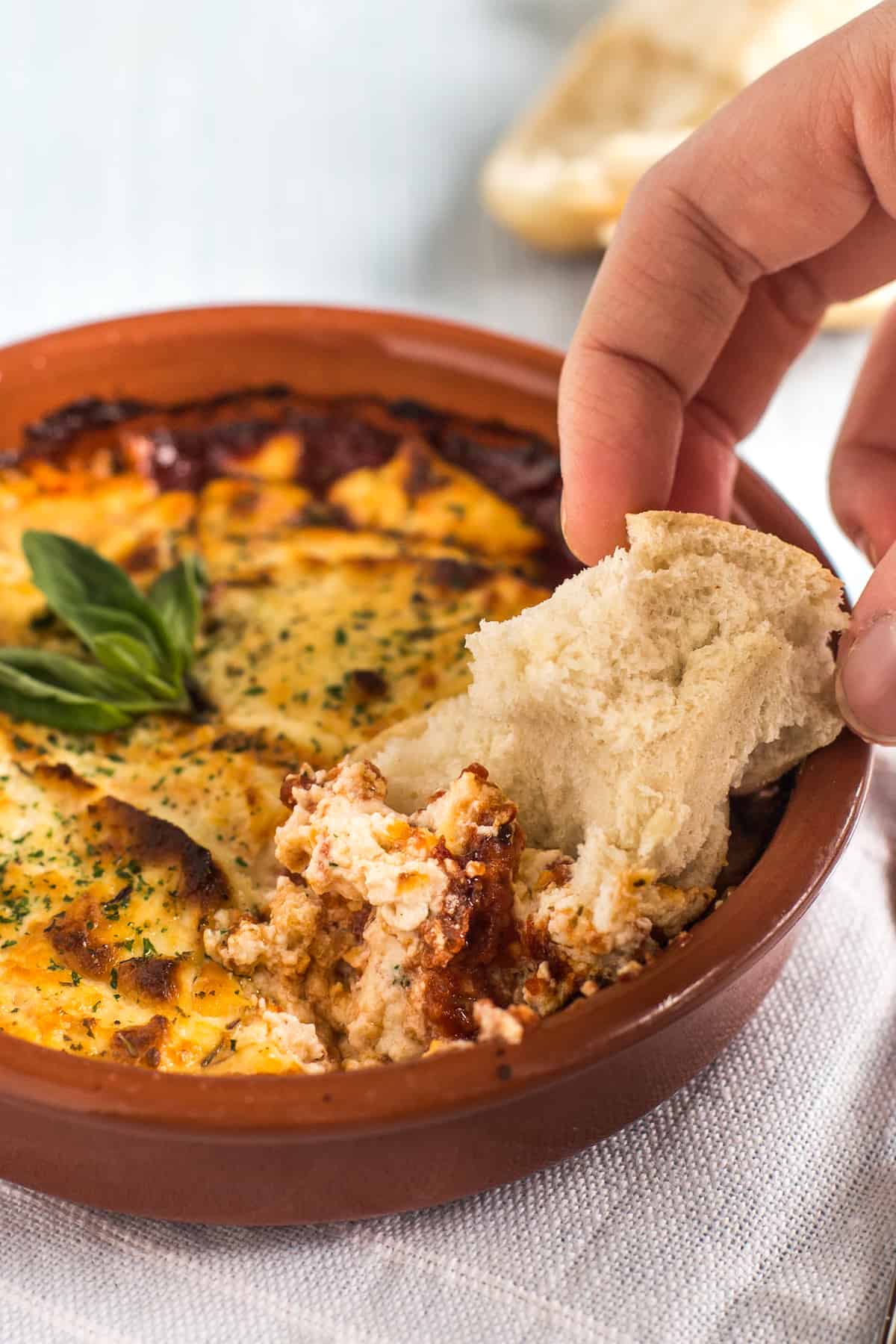 A hand dipping crusty bread into baked goat's cheese