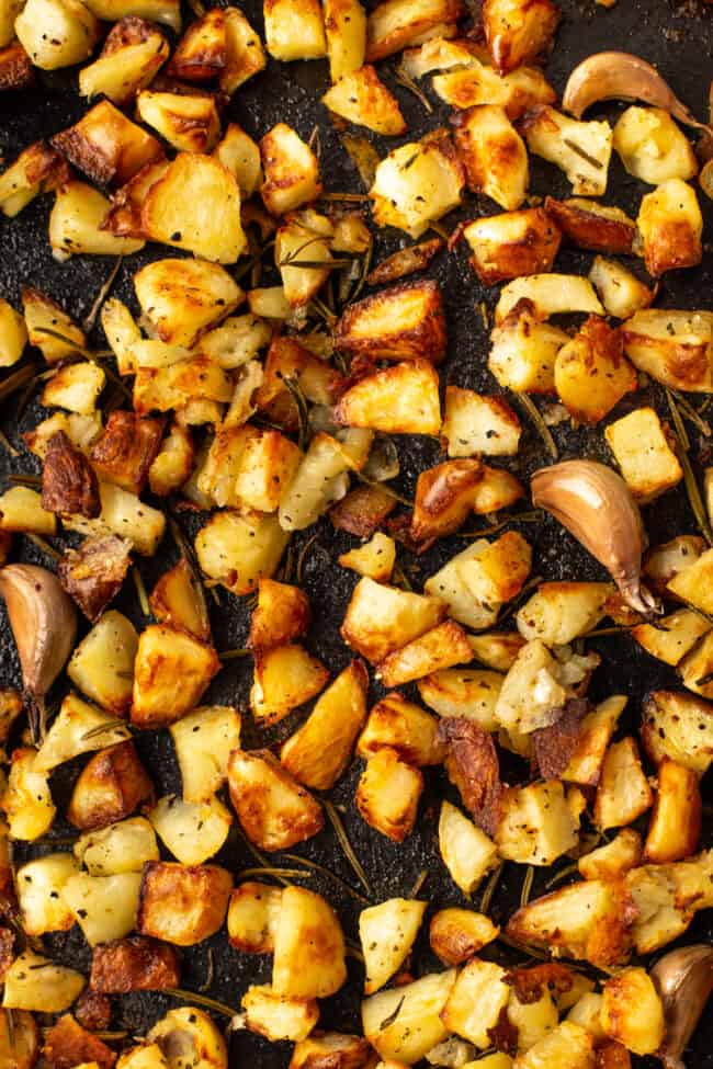 Close-up photo of Parmentier potatoes on a baking tray with cloves of garlic.