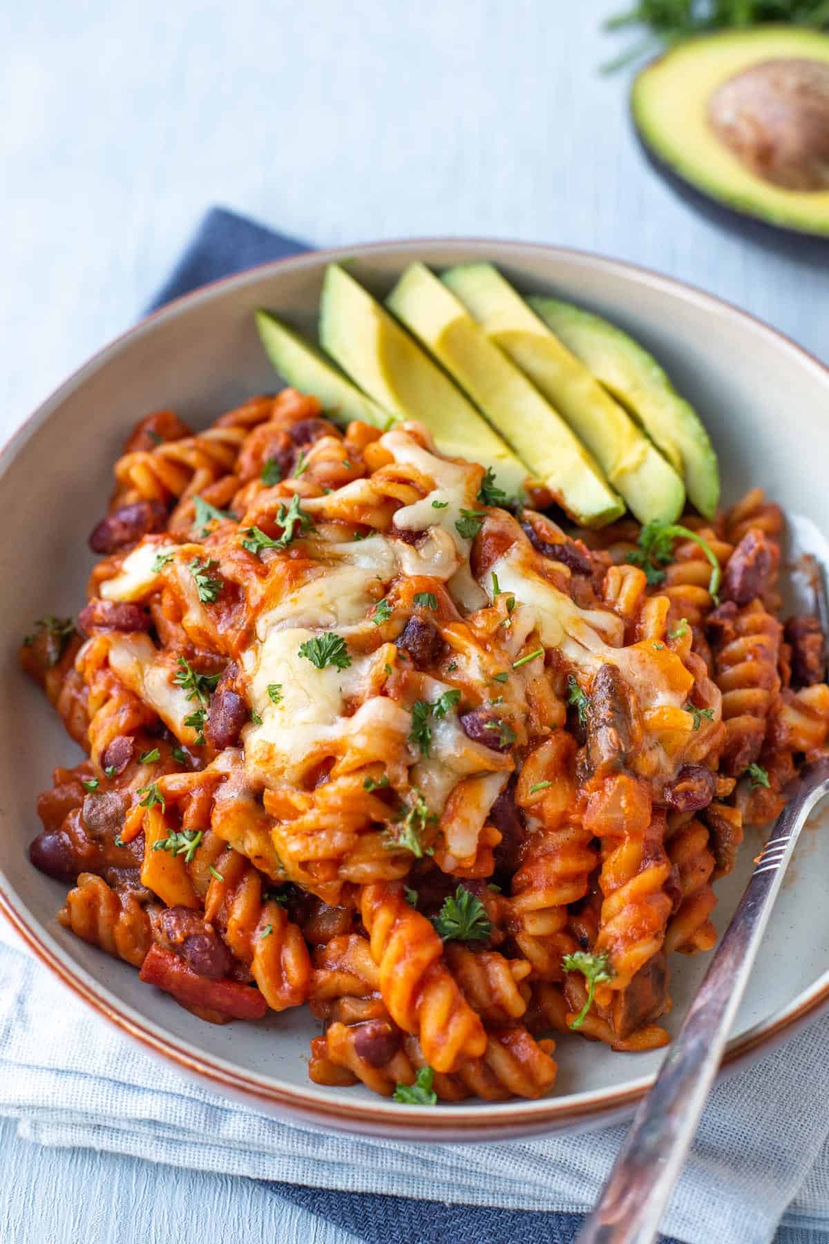 Vegetarian chilli mac in a bowl topped with cheese and avocado.