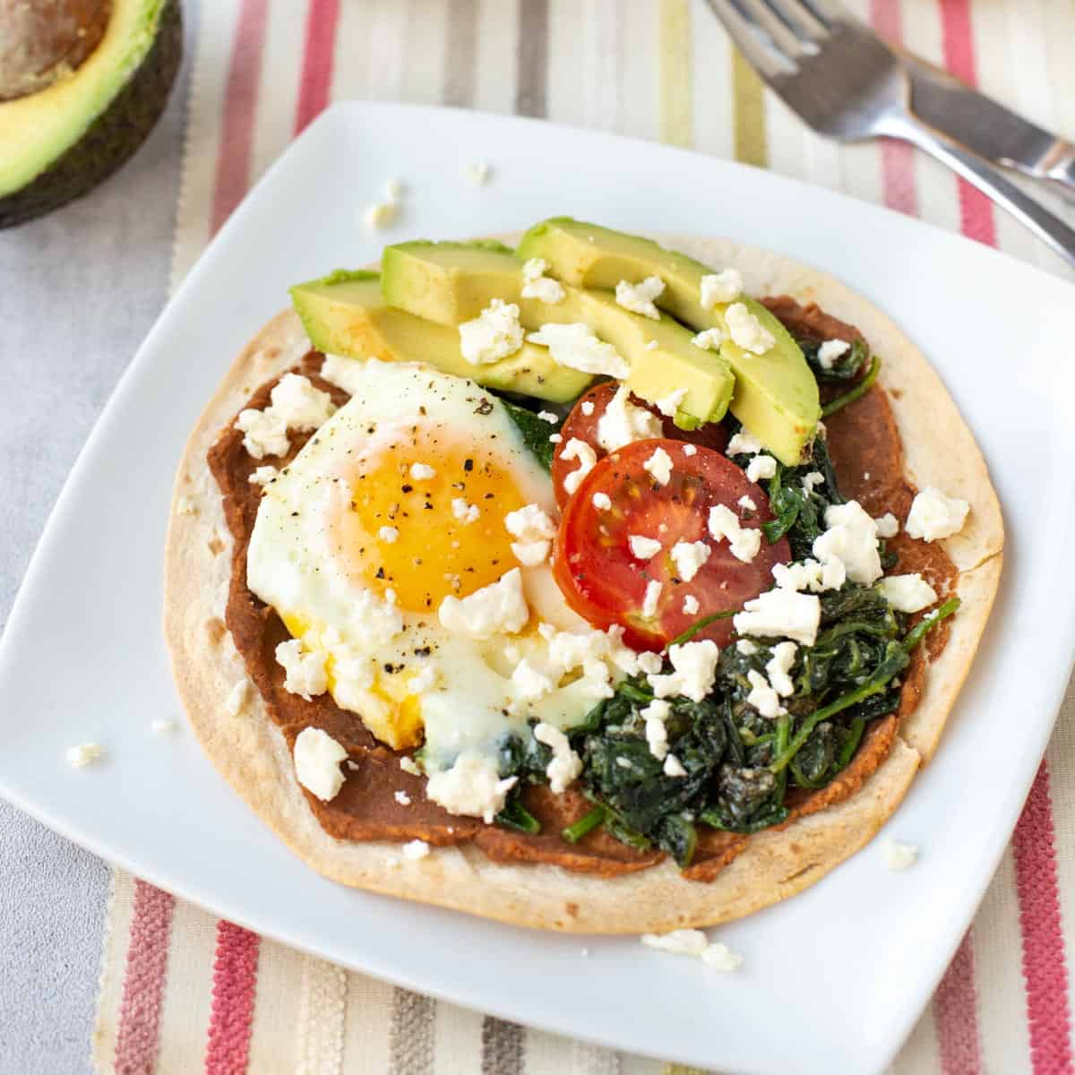 Breakfast tostada topped with a fried egg and feta cheese.