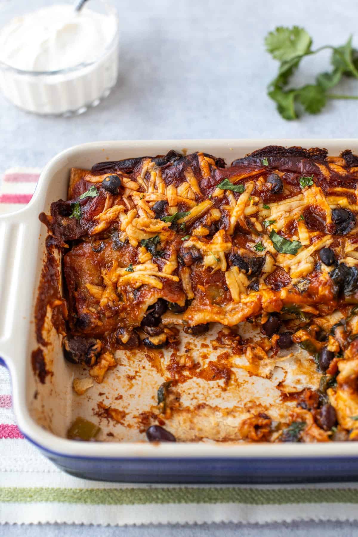 Cheesy black bean enchiladas in a baking dish with a portion removed.