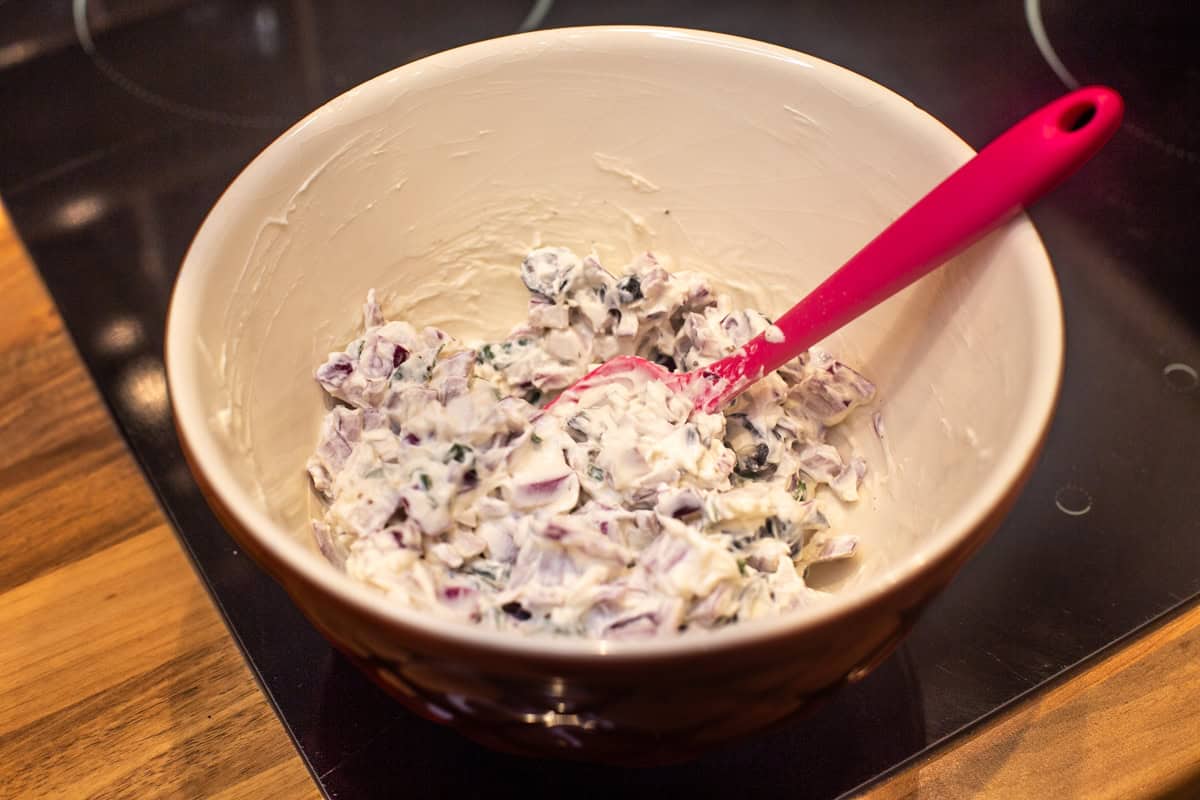 Cream cheese, red onion and olives mixed together in a bowl.