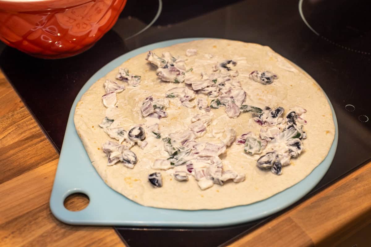 A tortilla wrap spread with cream cheese, red onion and olives.