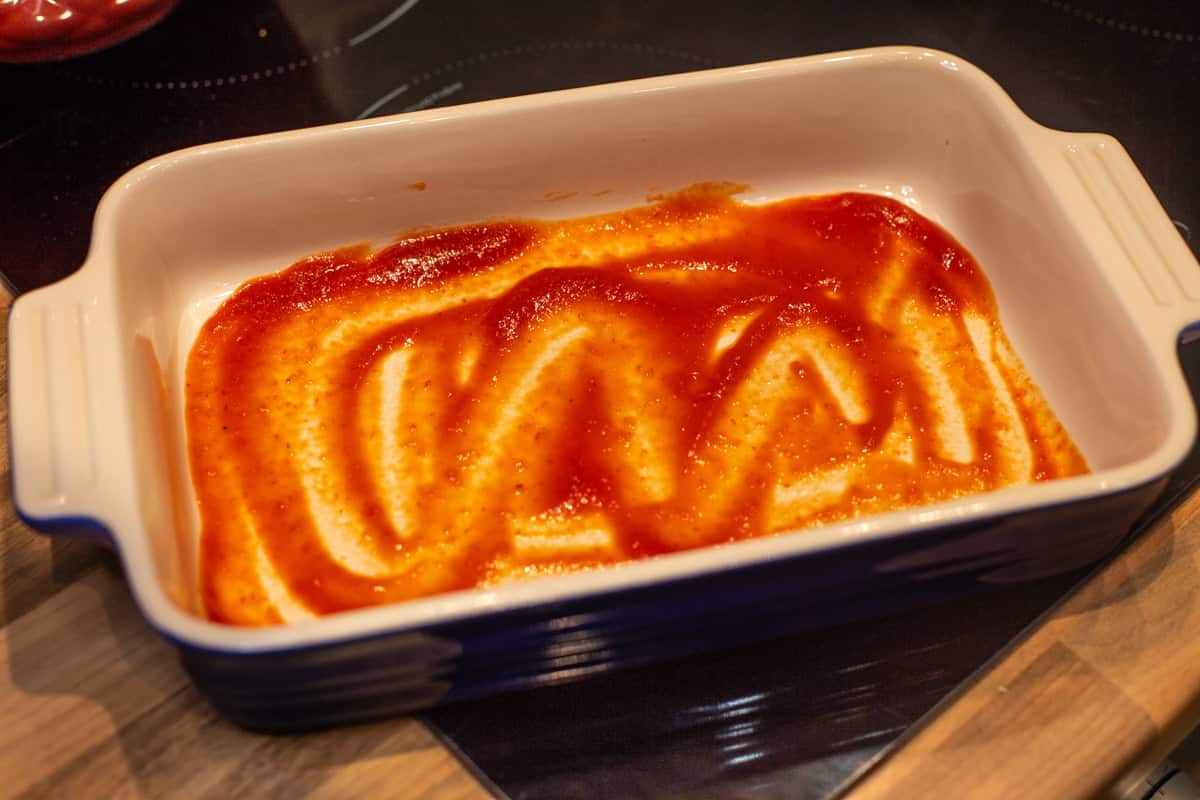 A thin layer of tomato sauce spread around the bottom of a baking dish.