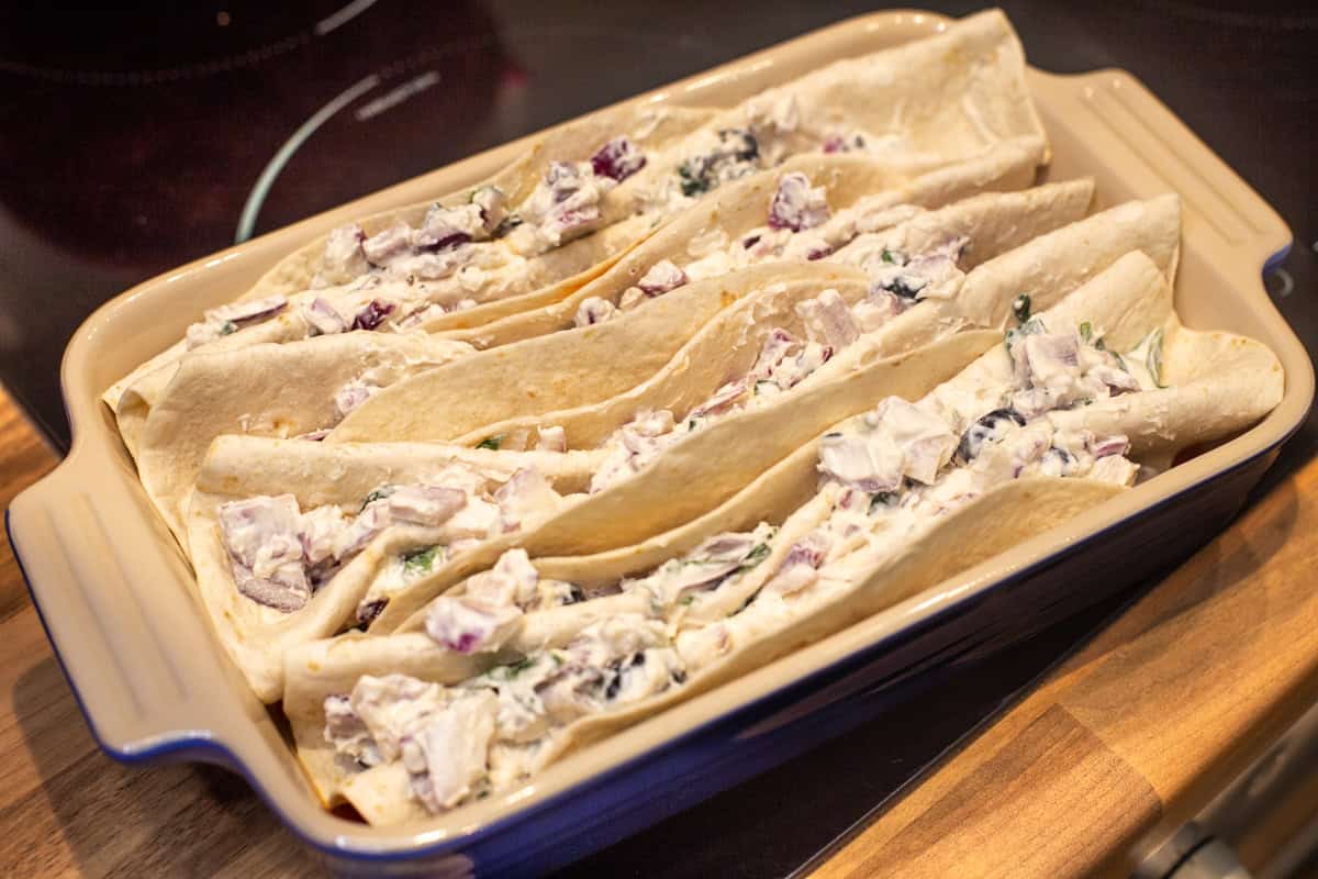 Zigzag folded tortillas stuffed with cream cheese in a baking dish.