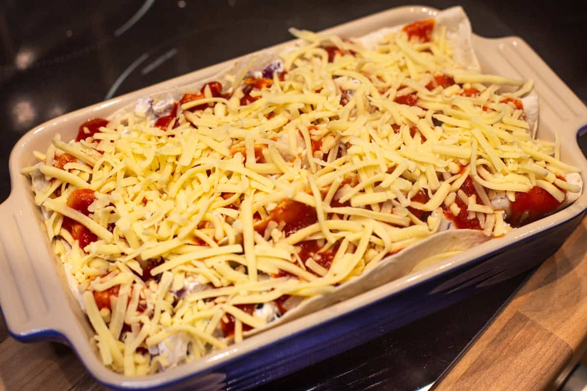 Unbaked creamy zigzag tortilla bake topped with grated cheese.