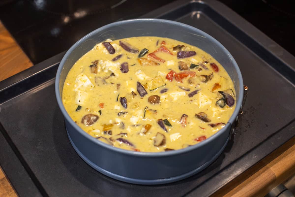 Uncooked crustless vegetable quiche in a springform cake tin.