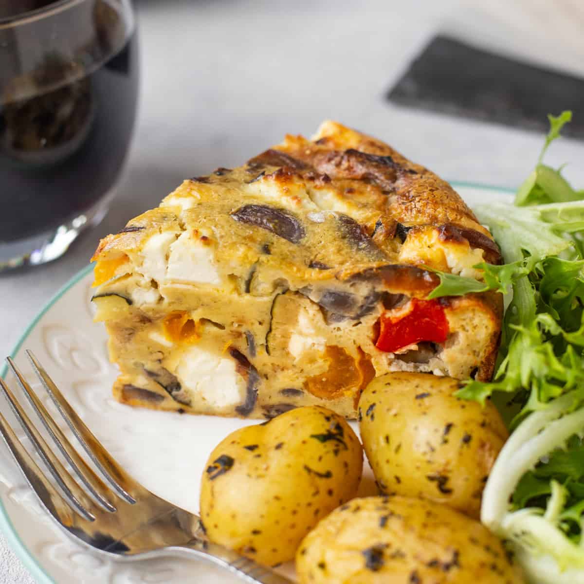 A slice of vegetable crustless quiche on a plate with potatoes and salad.