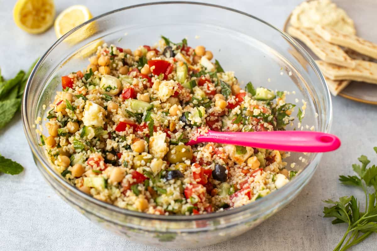 A large bowlful of tabbouleh salad with halloumi cheese and olives.