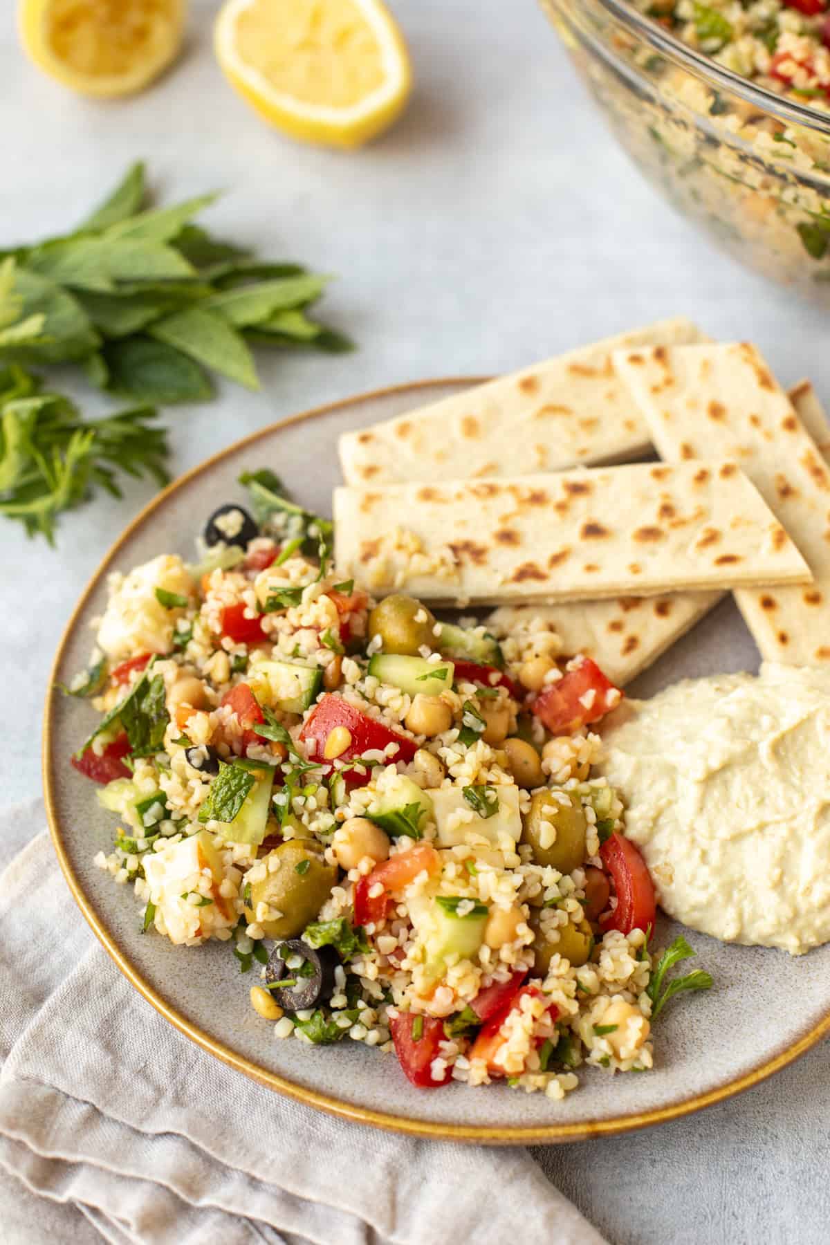 A portion of tabbouleh on a plate with hummus and pitta bread.