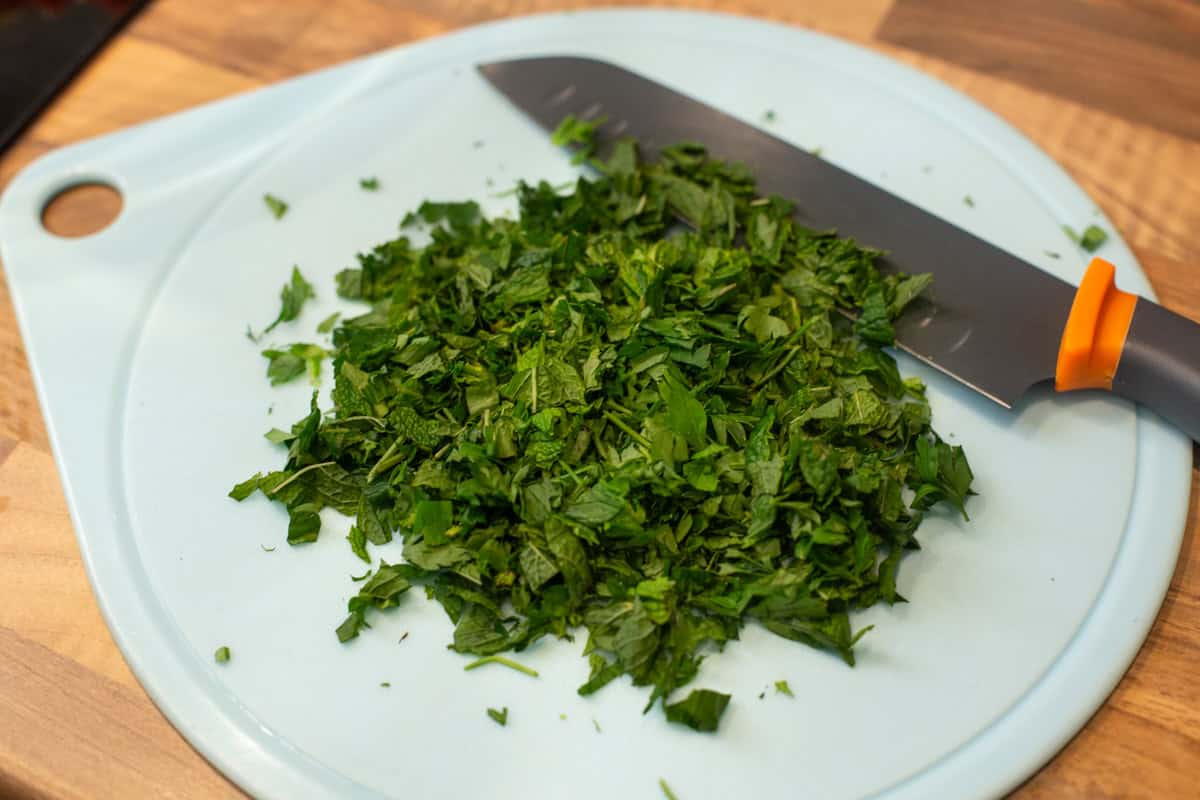 Chopped parsley and mint on a chopping board.