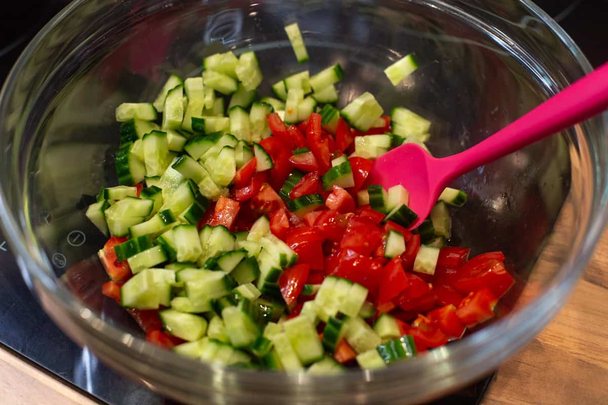 Chopped cucumber and tomatoes in a mixing bowl.