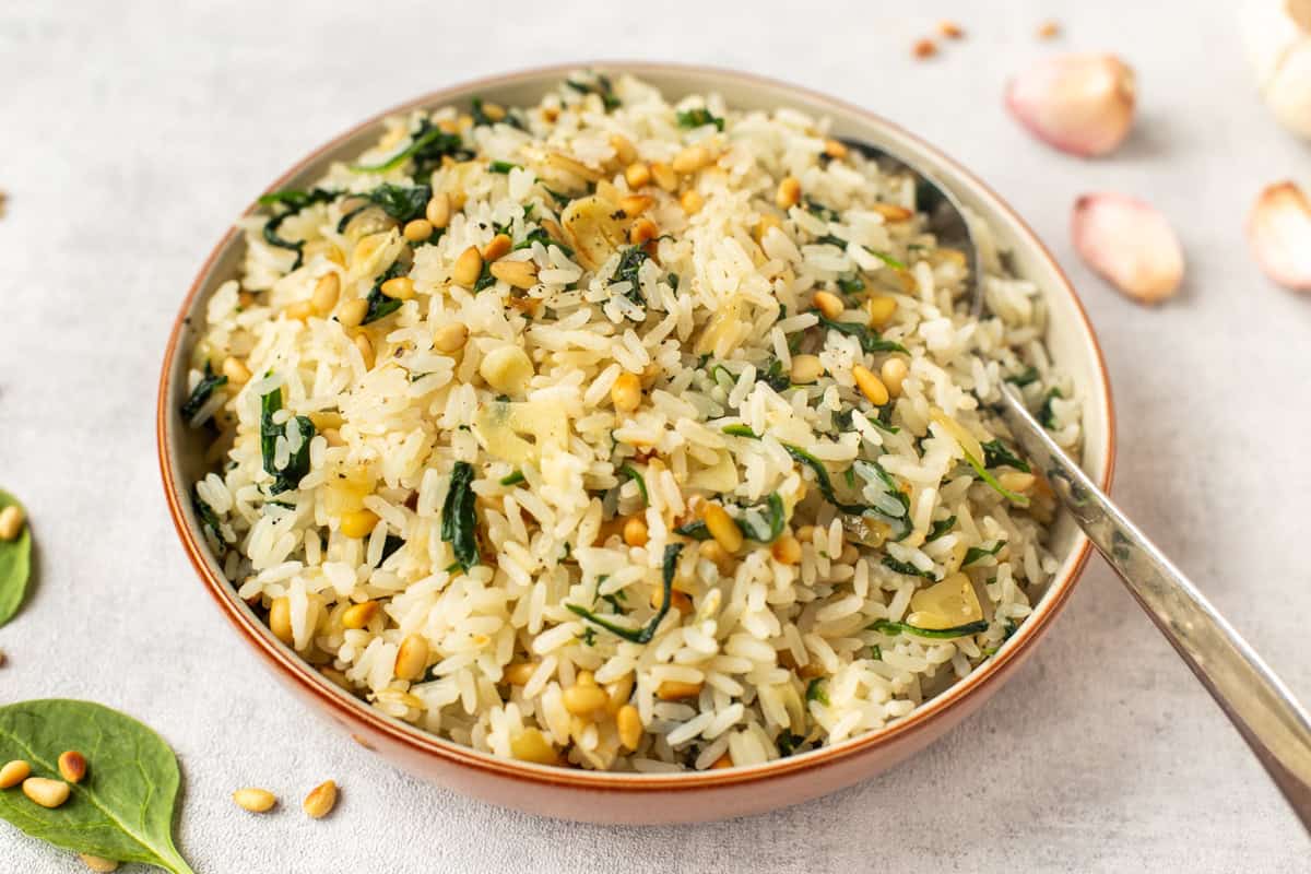 A bowl of garlic spinach rice topped with toasted pine nuts.