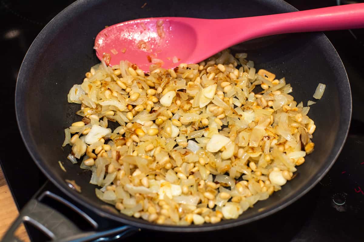 Fried onions, garlic and pine nuts in a frying pan.