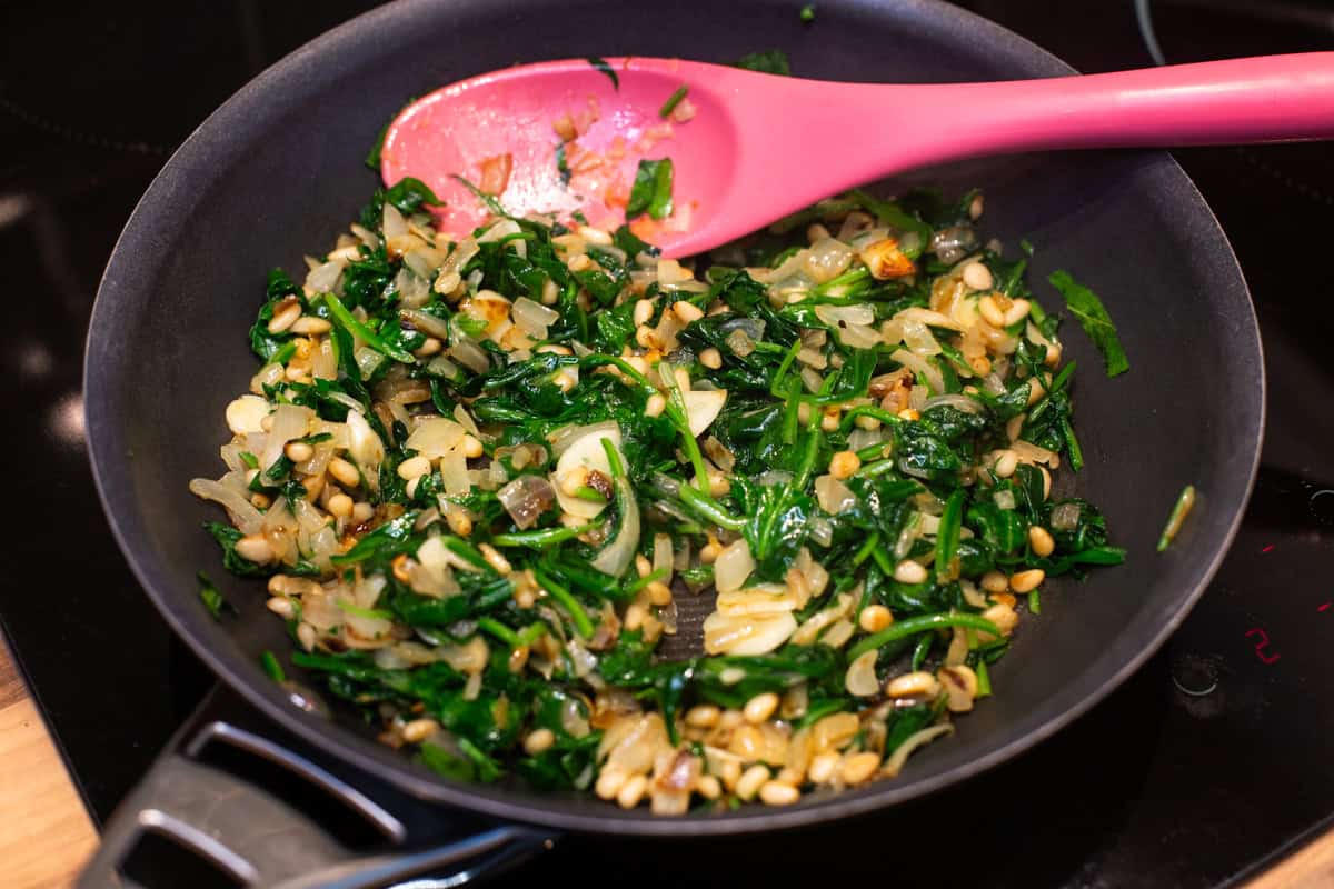 Sautéed spinach with garlic and pine nuts in a frying pan.