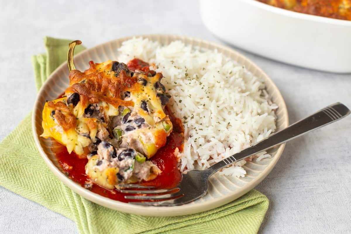 A yellow pepper stuffed with creamy ricotta and black beans on a plate with rice and tomato sauce.