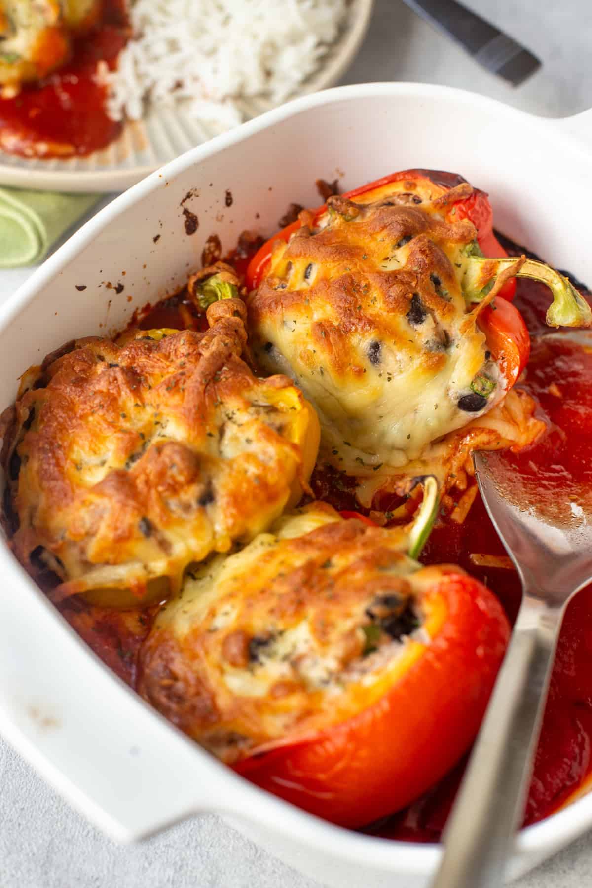 Three cheesy stuffed peppers in a baking dish, sitting on tomato sauce.