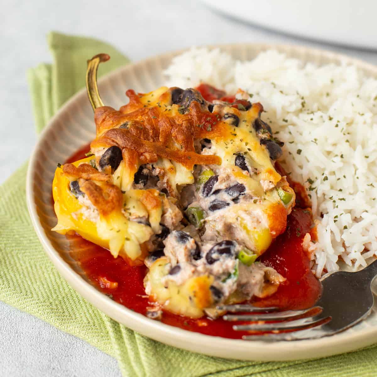 A yellow pepper stuffed with creamy ricotta and black beans on a plate with rice and tomato sauce.