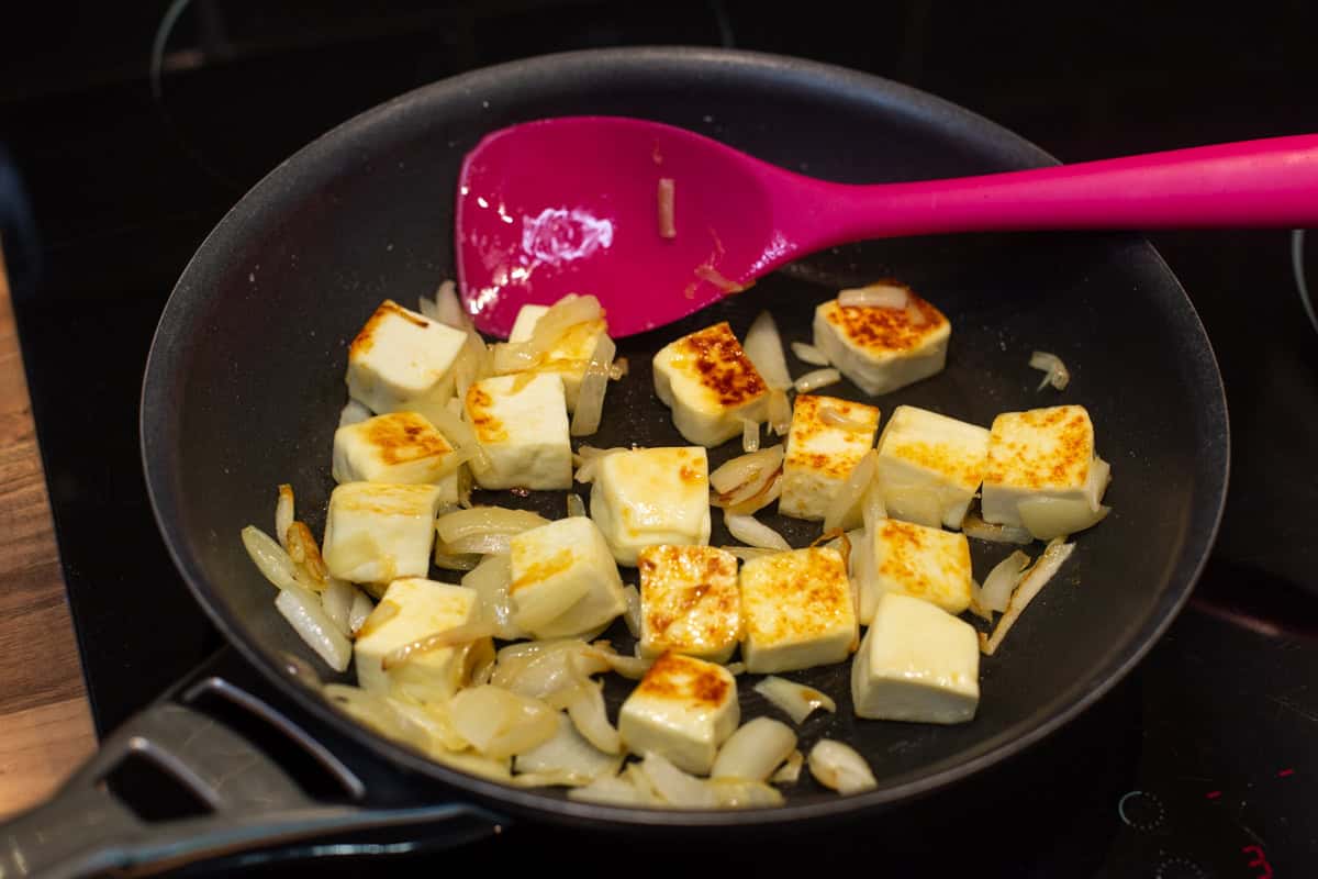 Paneer cheese and onions cooking in a frying pan.