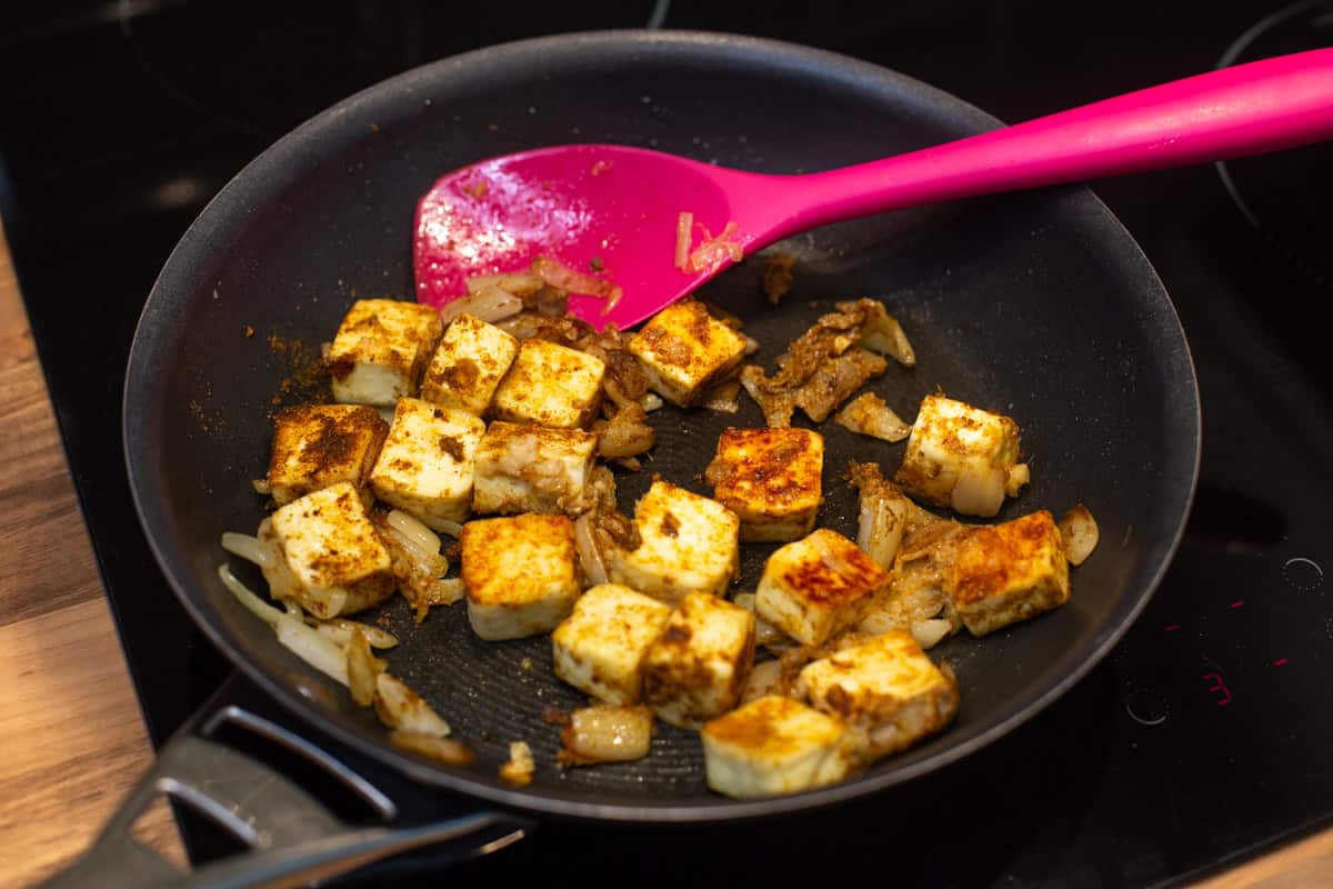 Spiced paneer and onions cooking in a frying pan.