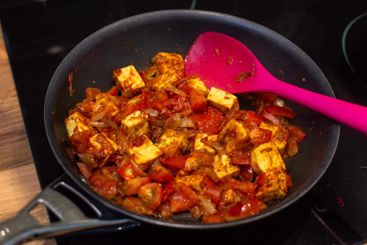 Paneer cooking in a rich tomato mixture in a frying pan.