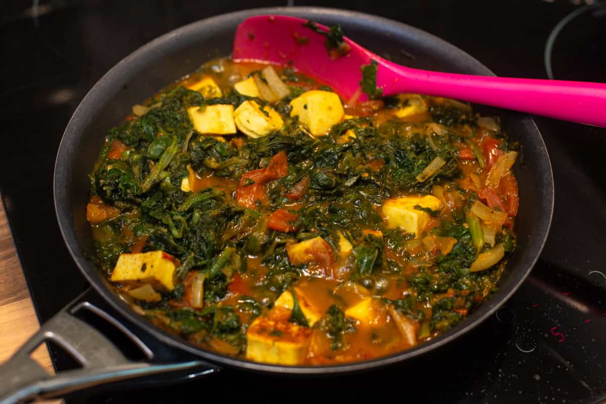 Saag paneer (spinach and paneer curry) cooking in a frying pan.