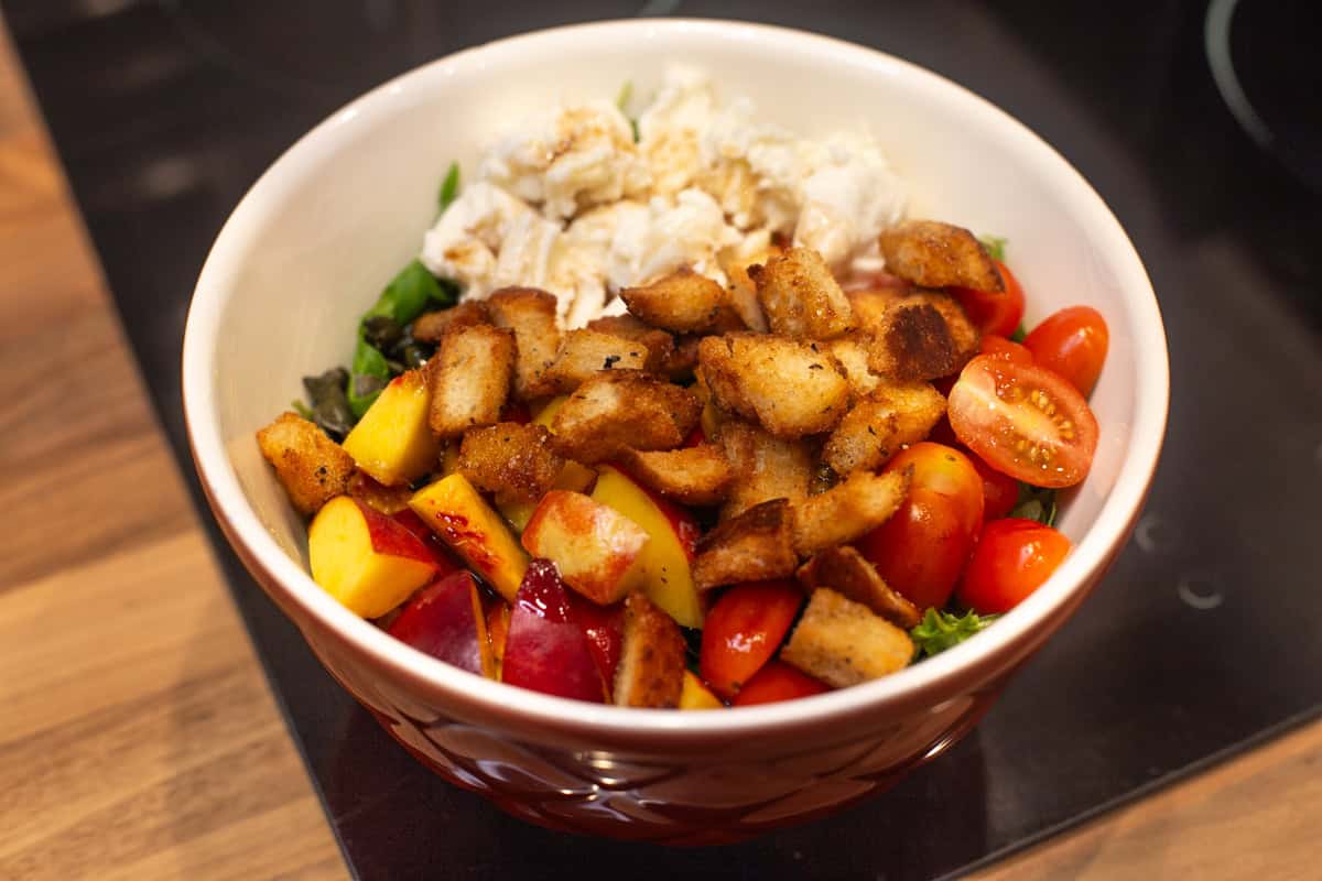 A mixing bowl with peaches, mozzarella and homemade croutons.