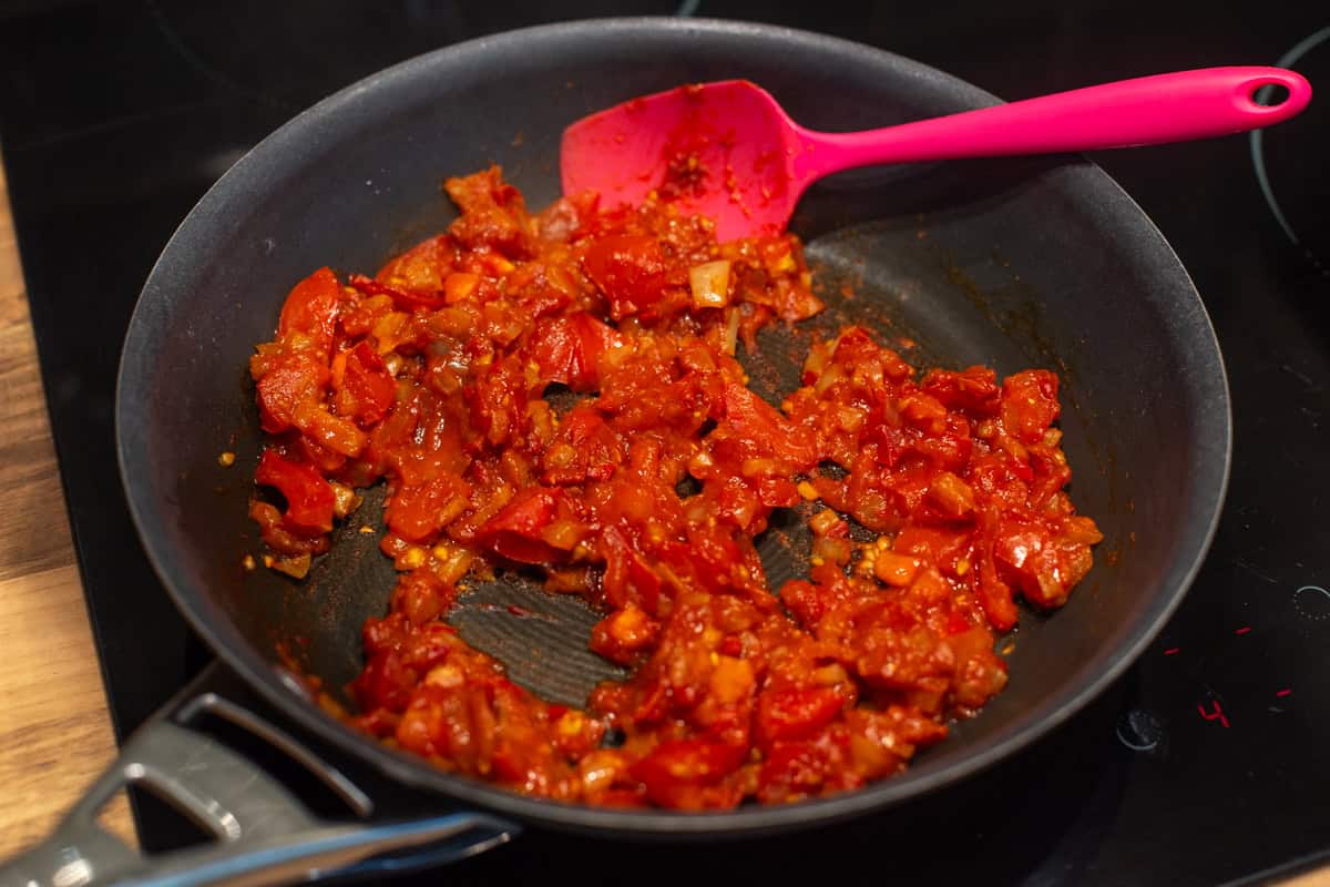 Rich tomatoes and onions cooking in a frying pan.