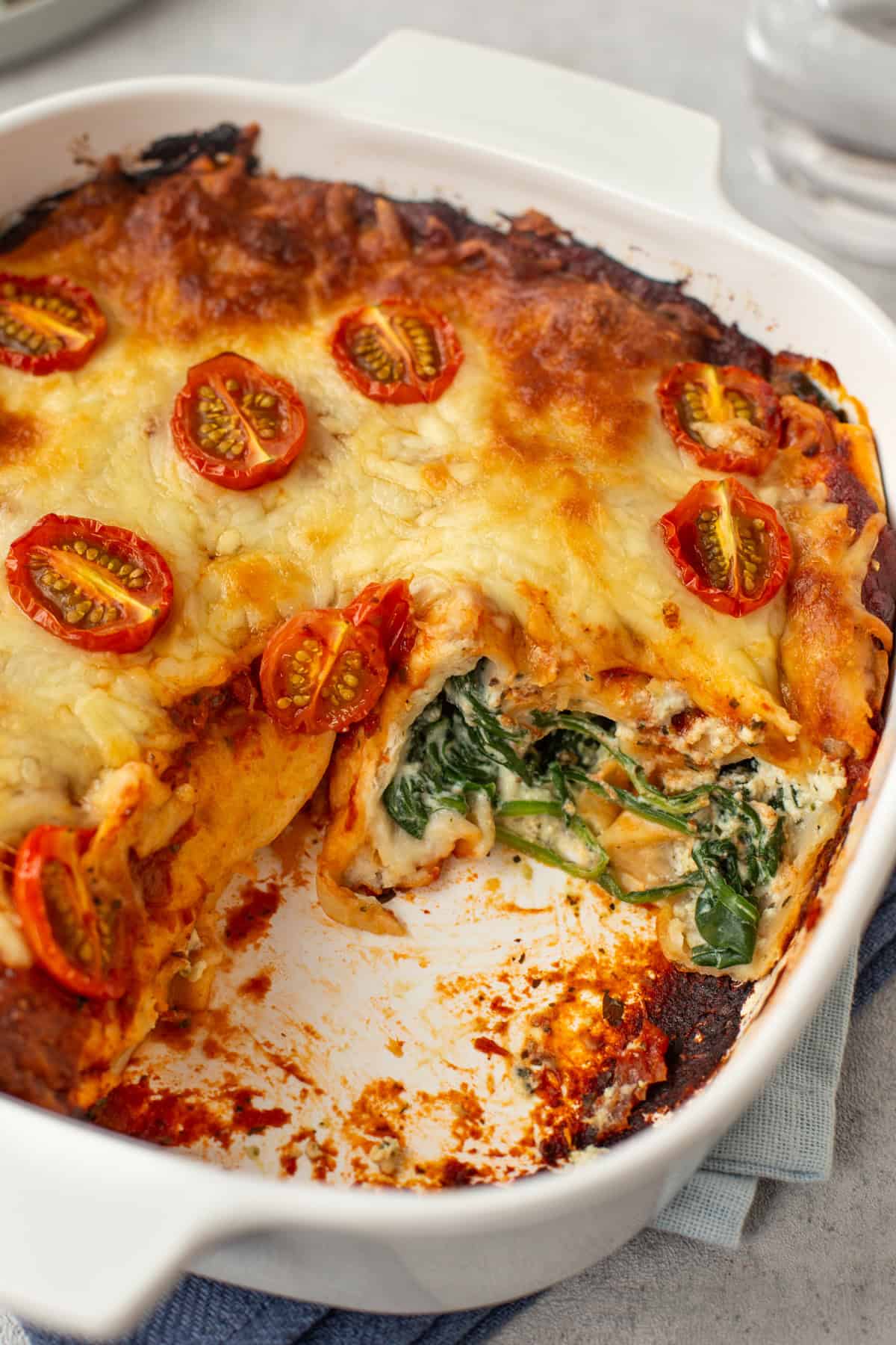 A baking dish of spinach and ricotta enchiladas with a portion removed.