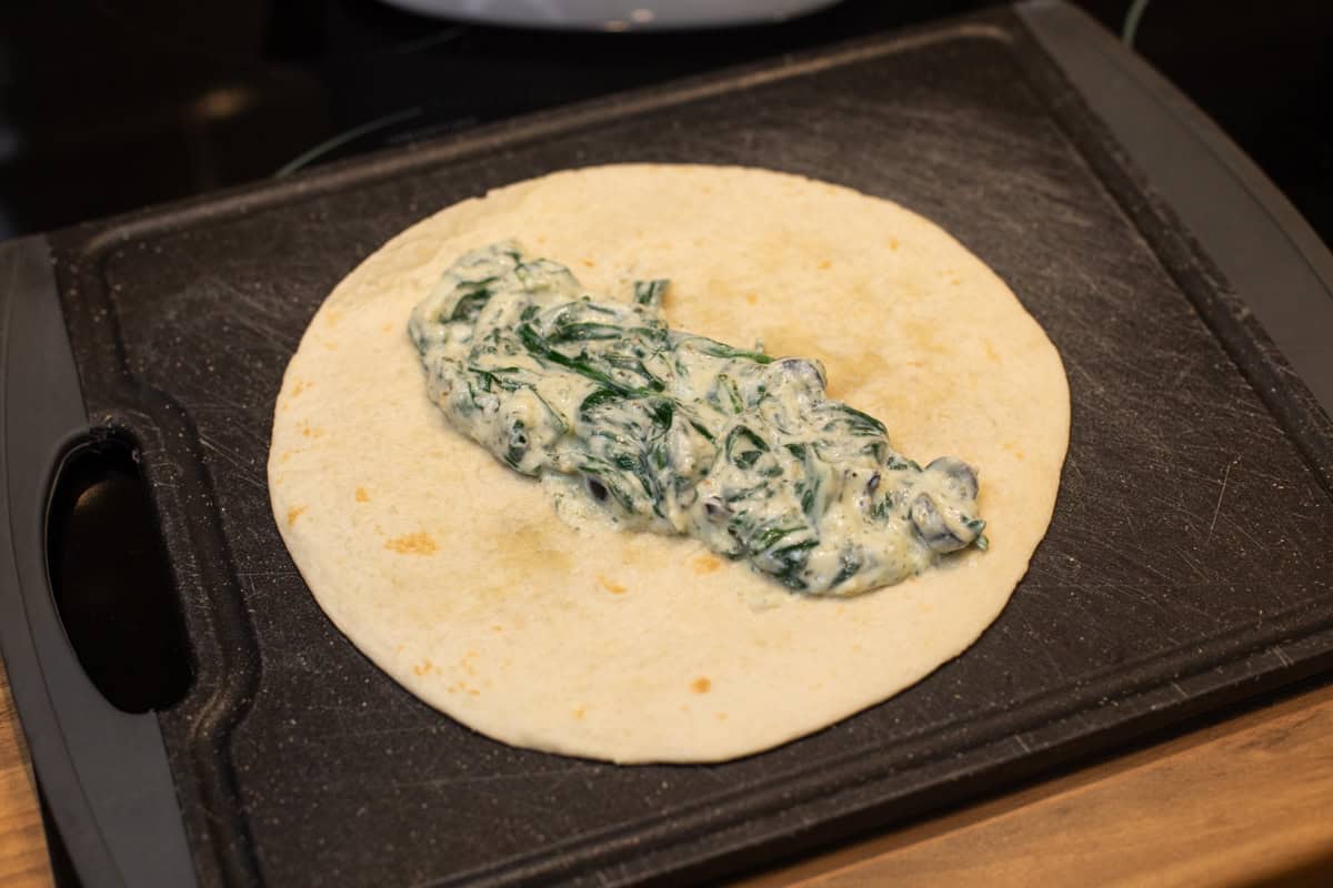 A flour tortilla on a chopping board with creamy spinach on top.