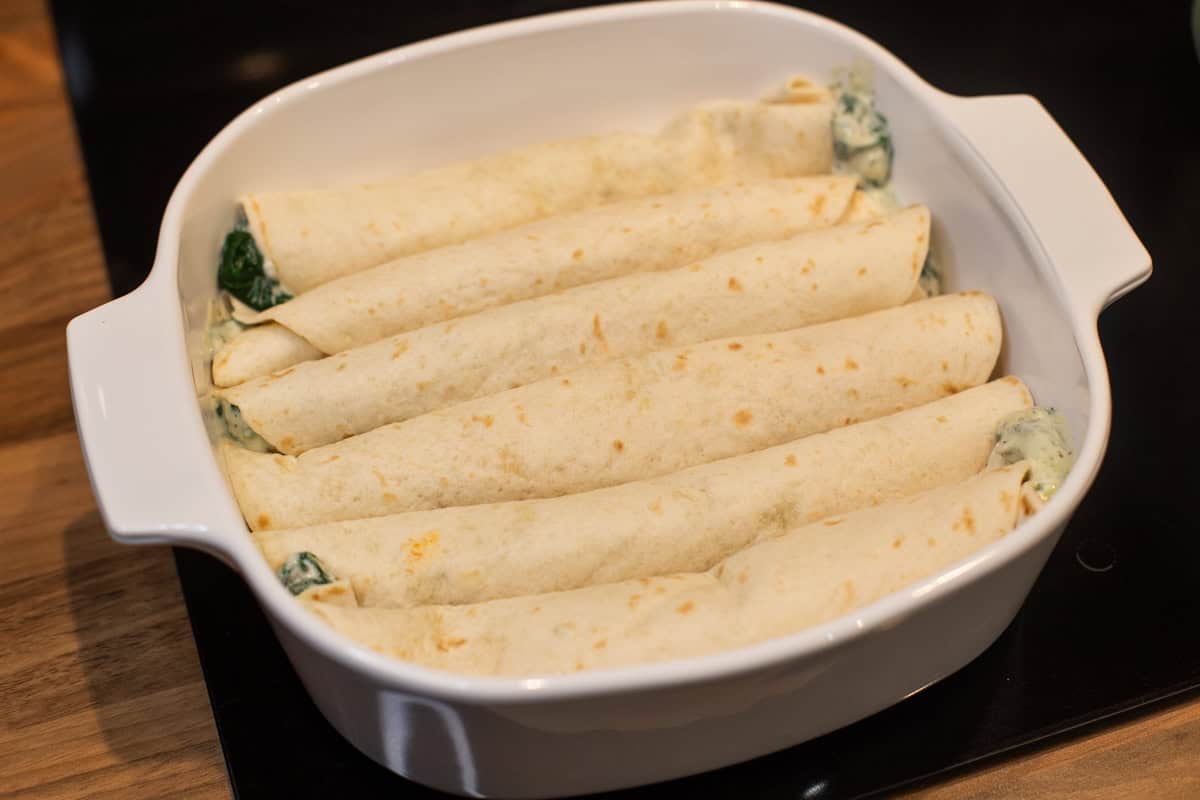 Rolled tortillas stuffed with creamy spinach and laid in a baking dish.