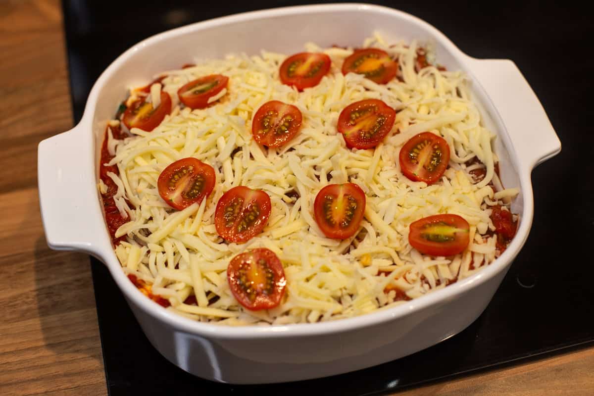 Uncooked enchiladas topped with mozzarella and tomatoes.