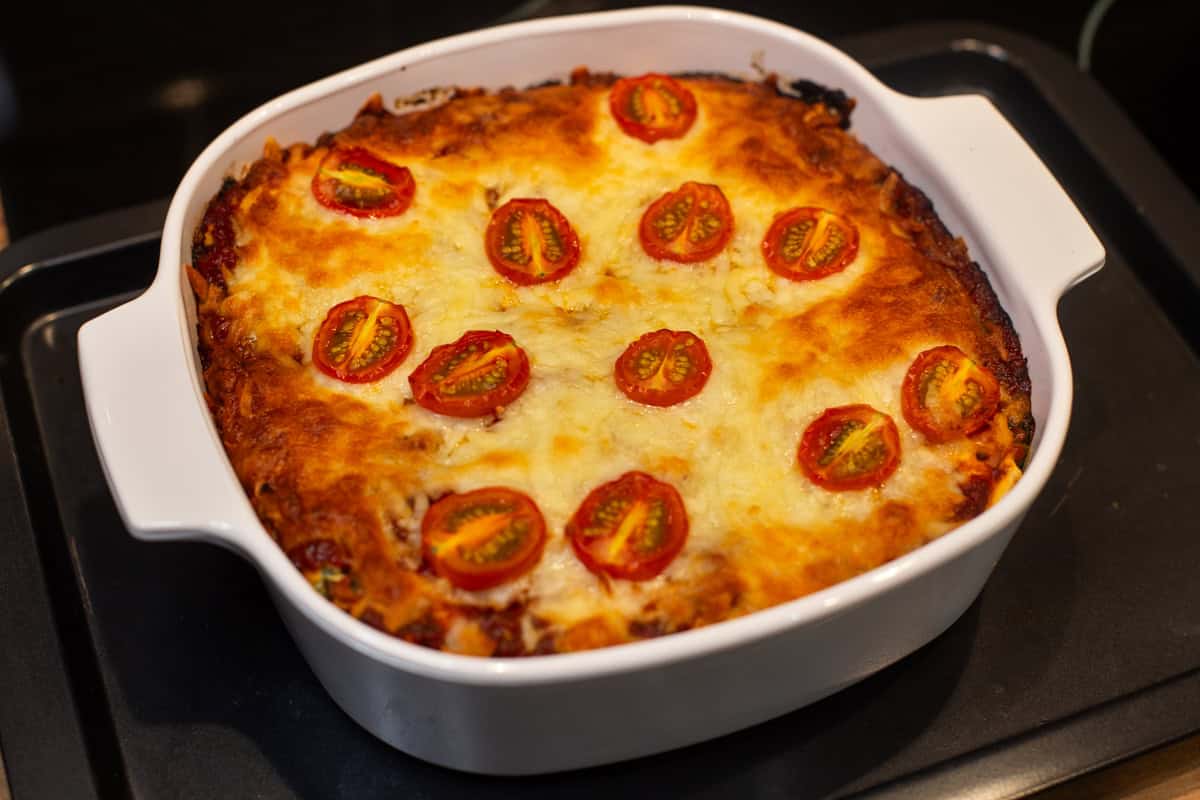 A baking dish of spinach enchiladas topped with crispy cheese and cherry tomatoes.