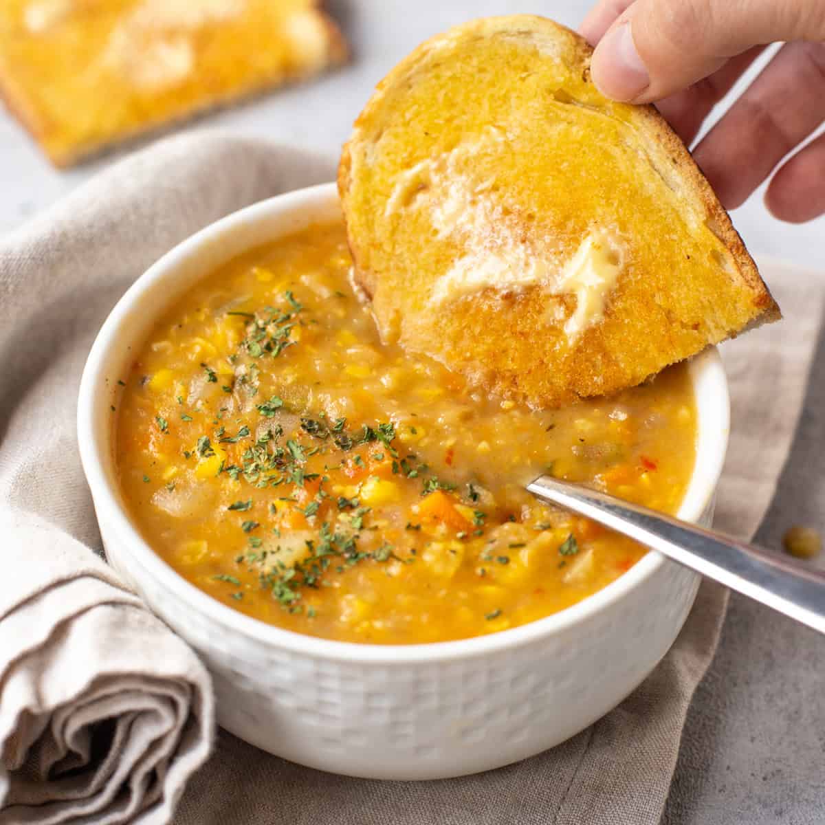 Buttered toast being dipped into a bowl of coconut corn chowder.