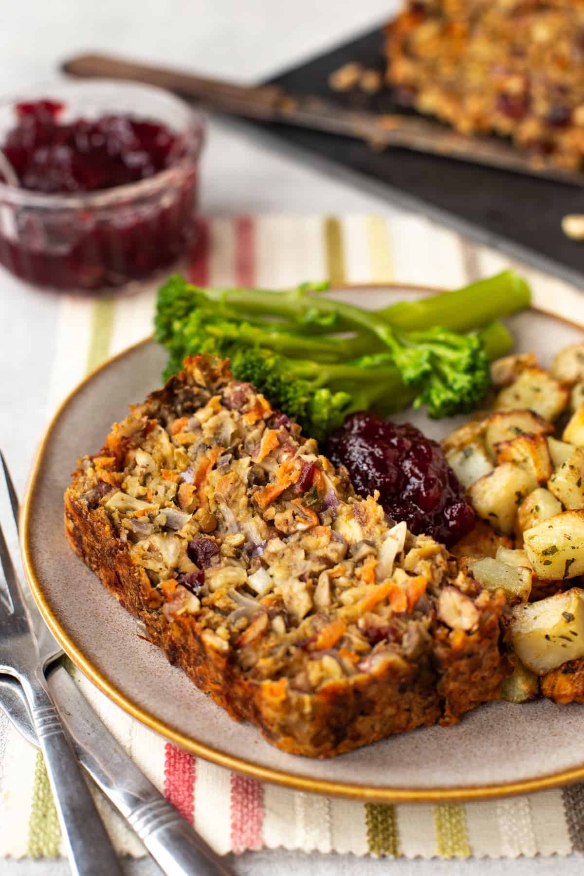 A slice of nut roast on a plate with broccoli and potatoes.