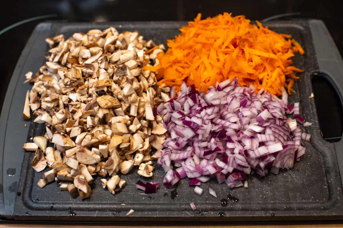 Finely chopped mushrooms, red onion and carrot on a cutting board.