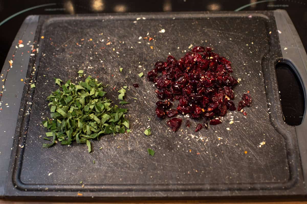 Chopped sage and dried cranberries on a cutting board.