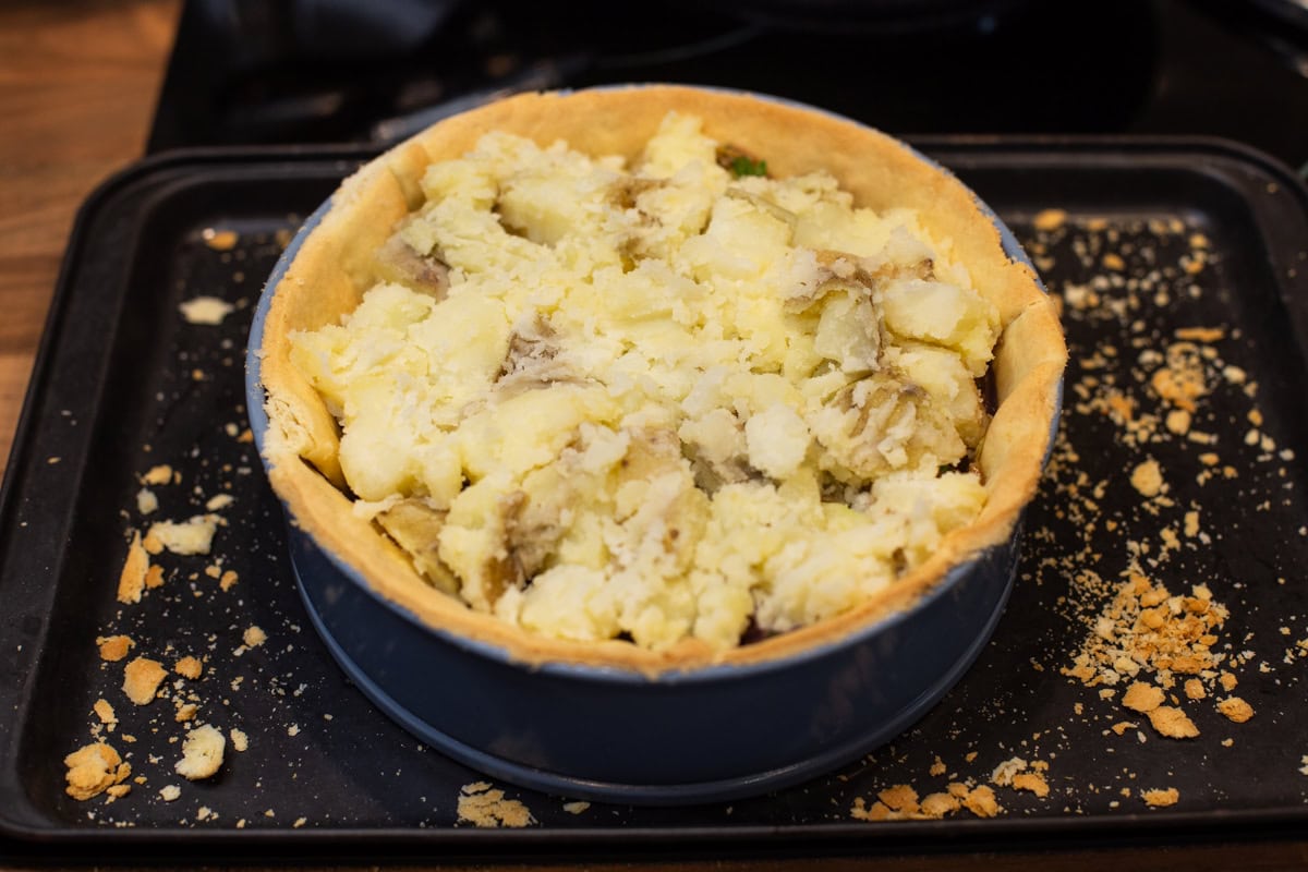 A pastry case topped with crushed potatoes.