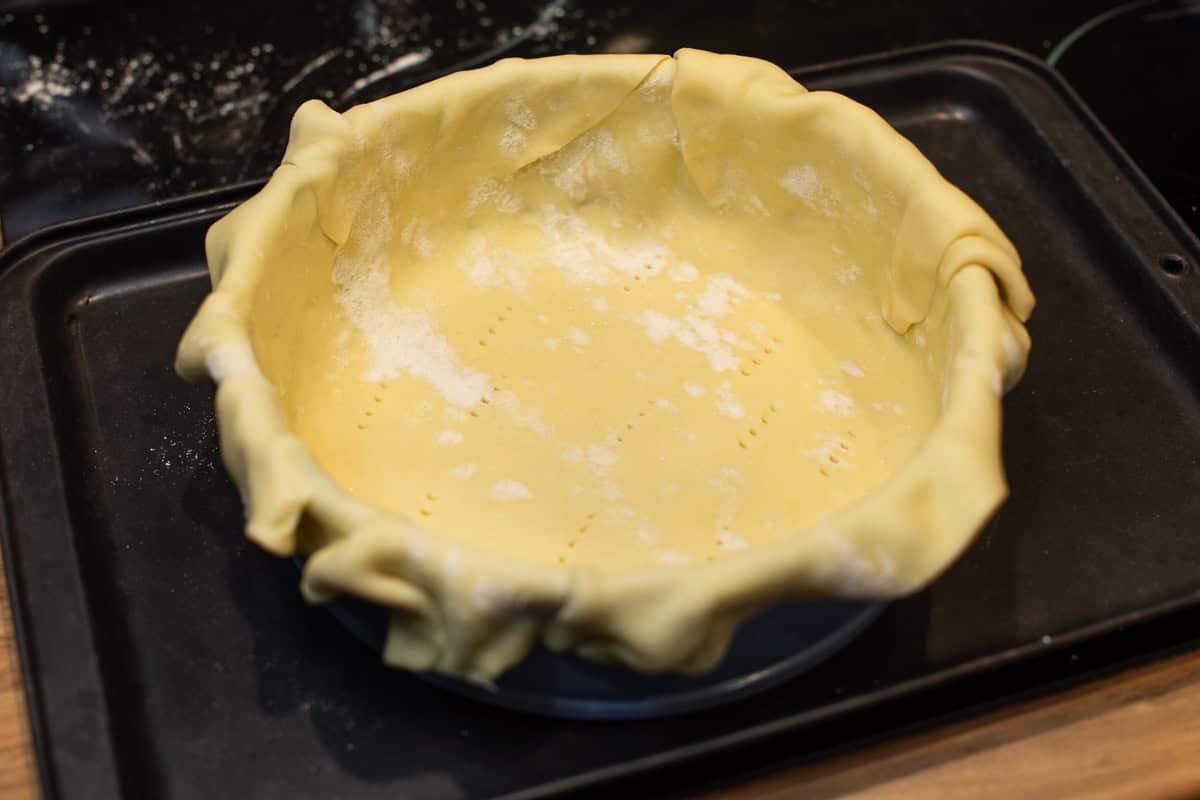 Uncooked shortcrust pastry draped over a cake tin.