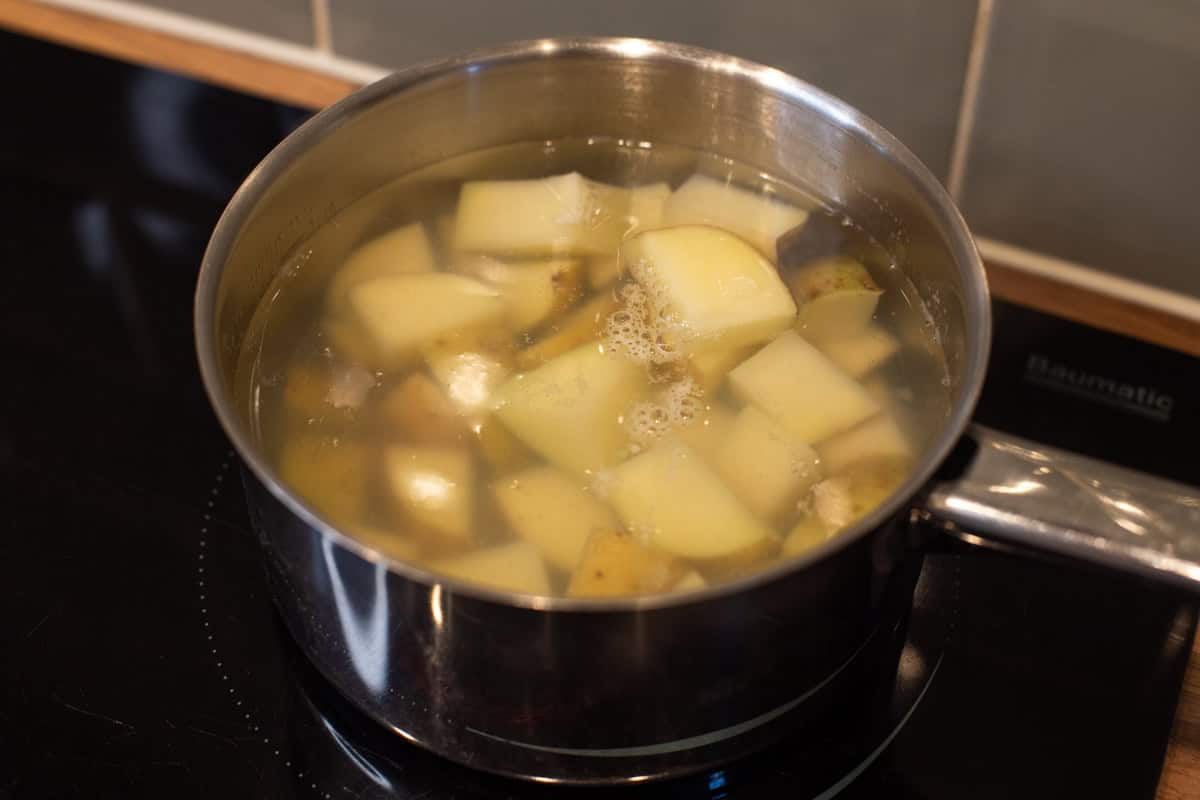 Pieces of potato cooking in a pan of water.