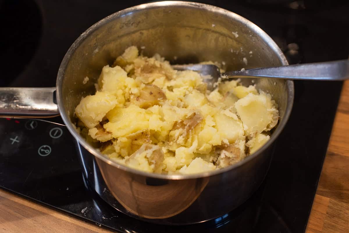 Roughly crushed boiled potatoes in a saucepan.