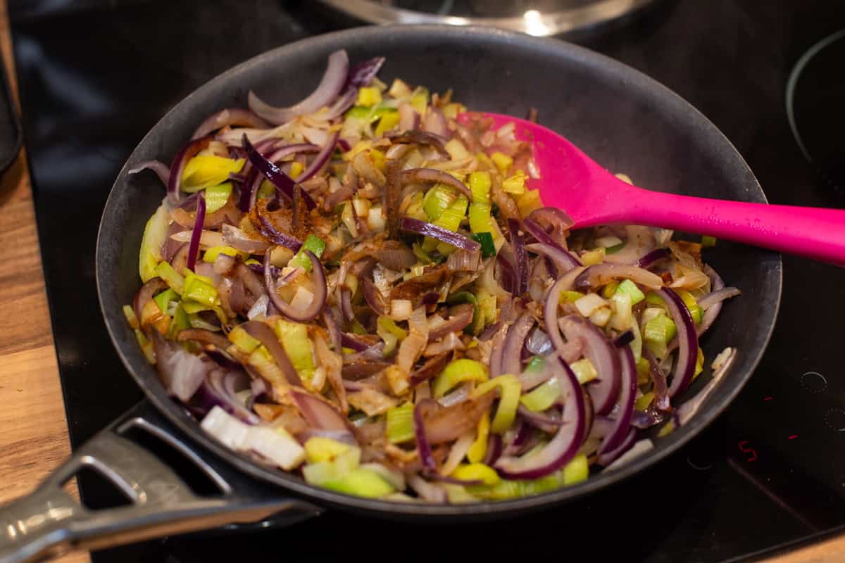 Sautéed leeks and red onion in a frying pan.