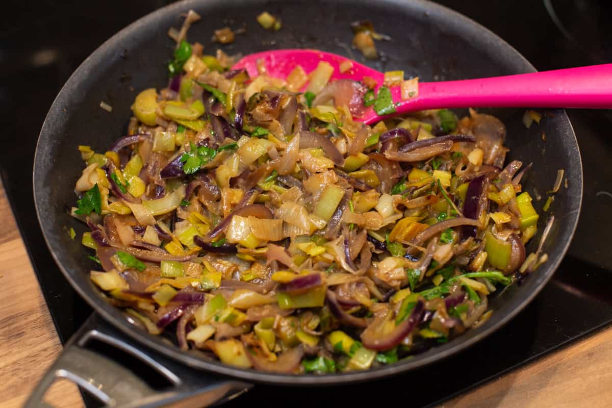 Sautéed leeks and red onion in a frying pan.