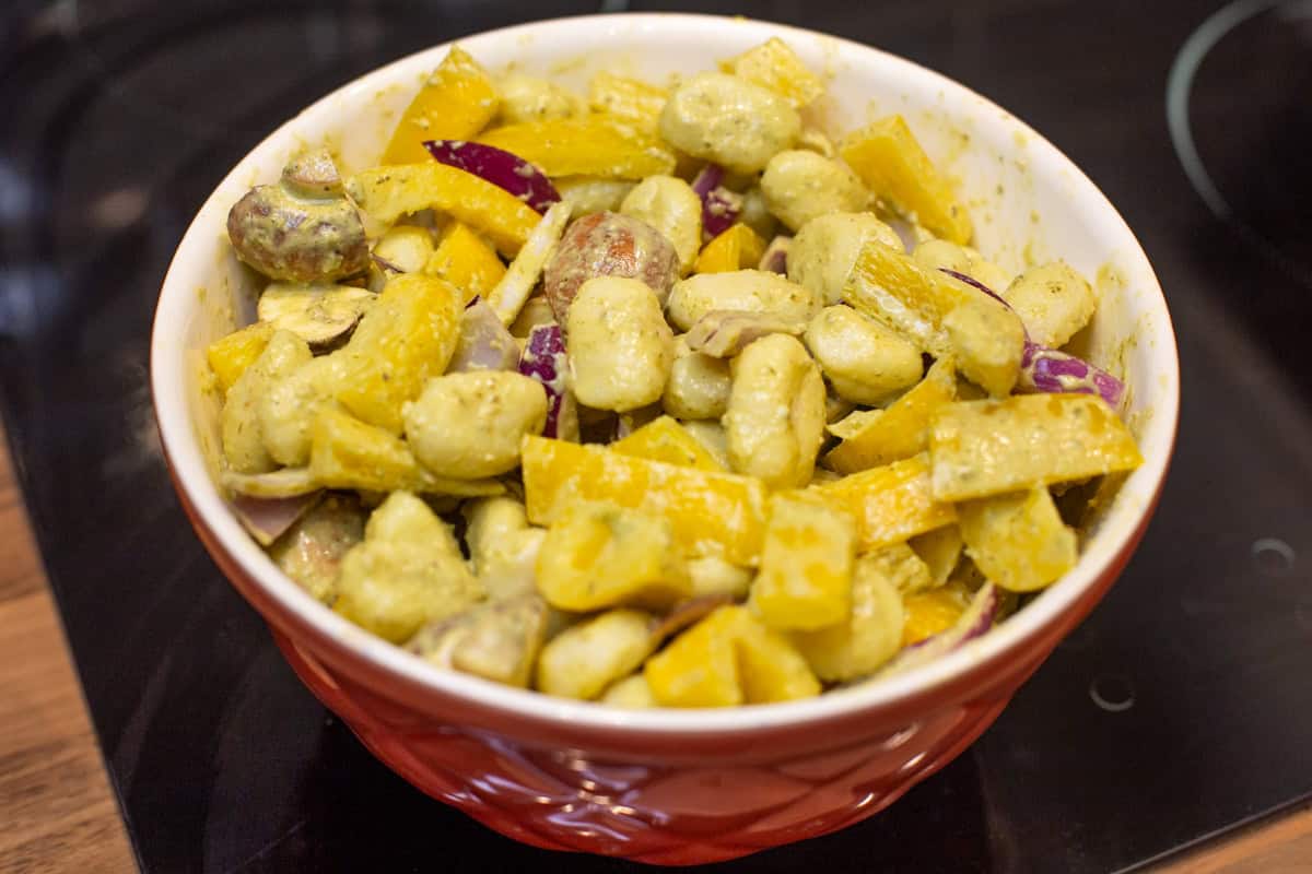 Gnocchi and raw vegetables coated in pesto in a mixing bowl.