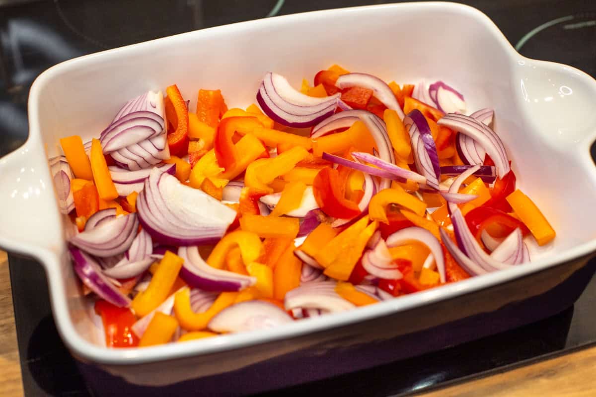 Chopped peppers and red onion in a large baking dish.