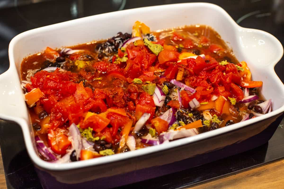 Uncooked rice, beans, vegetables and tomatoes in a baking dish.