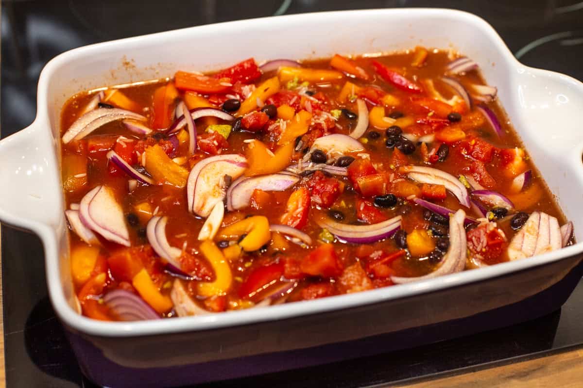 Uncooked rice, beans, vegetables and tomatoes in a baking dish.