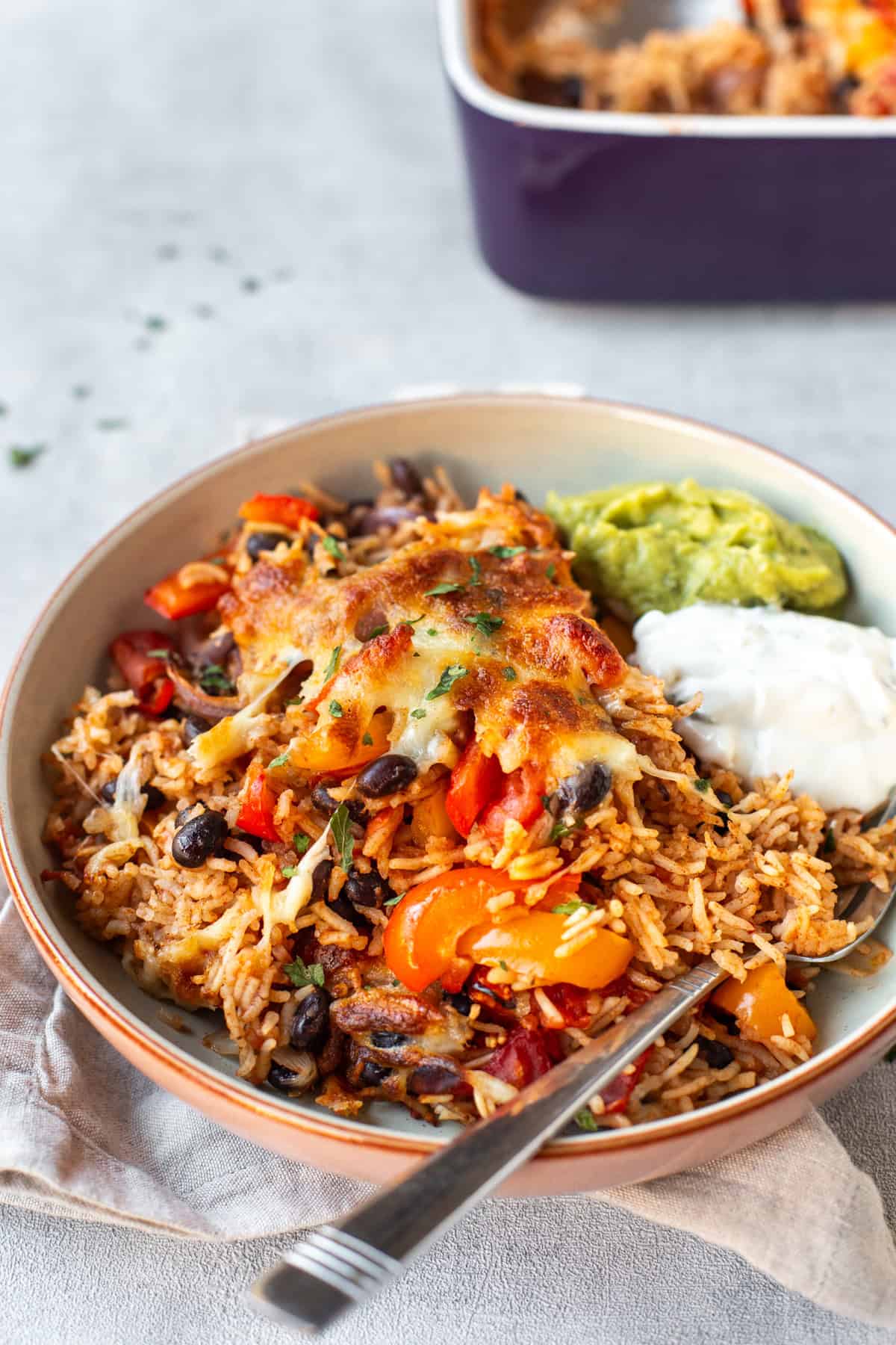 A portion of fajita baked rice with guacamole and sour cream.